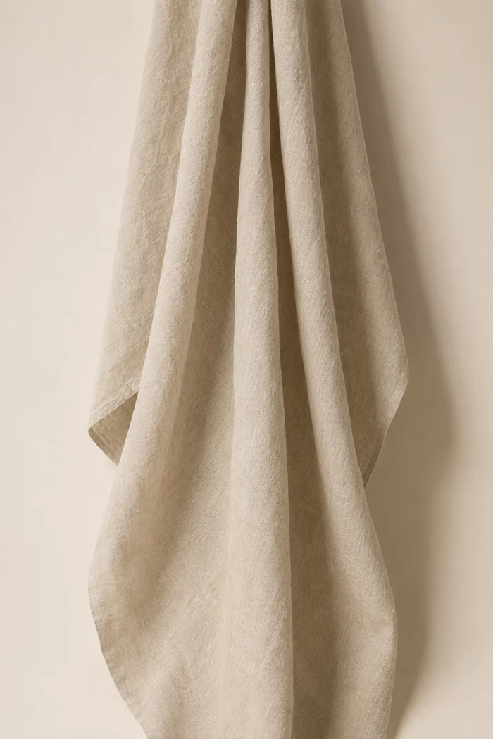 A narrow panel of washed linen hanging free, falling in wide dry folds.
